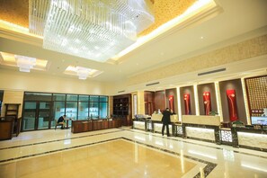 A spacious lobby with a high ceiling, a large chandelier, and a reception desk with a red decorative element.