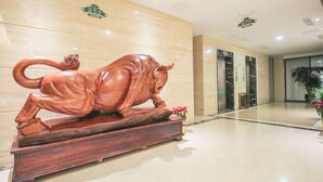 Un vestíbulo con una escultura de toro de madera sobre un pedestal, paredes de mármol y dos ascensores.