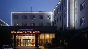Exterior del Hotel New Knight Royal, de diseño moderno, con una entrada destacada y una bandera en el edificio.
