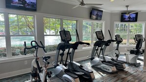 A gym with multiple exercise bikes and treadmills, large windows with a view of a lake, and two TVs mounted on the wall. - A peaceful Lake view by The Battery (Smyrna)