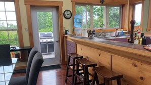 A kitchen with a wooden bar, stools, a sink, and a view of the outdoors. - Beachfront Guest Cottage in Antigonish (Antigonish)