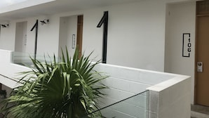 Um edifício moderno com portas numeradas, guarda-corpo de vidro e um vaso de planta.