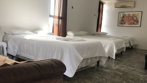 Quarto de hotel com três camas, uma cadeira marrom e um aparelho de ar condicionado na parede.