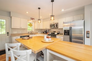 A modern kitchen with white cabinets, a wooden island, stainless steel appliances, and pendant lighting. - Spacious family-friendly chalet w/fenced dog run & large deck near the lake/Wisp (Oakland)