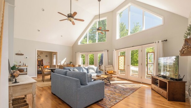 Ein geräumiges Wohnzimmer mit einer großen Couch, Holzböden, Deckenventilatoren und großen Fenstern.
