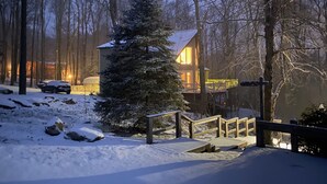 Eine verschneite Landschaft mit einer Holzhütte, einem mit Schnee bedeckten Baum und einem Holzzaun.
