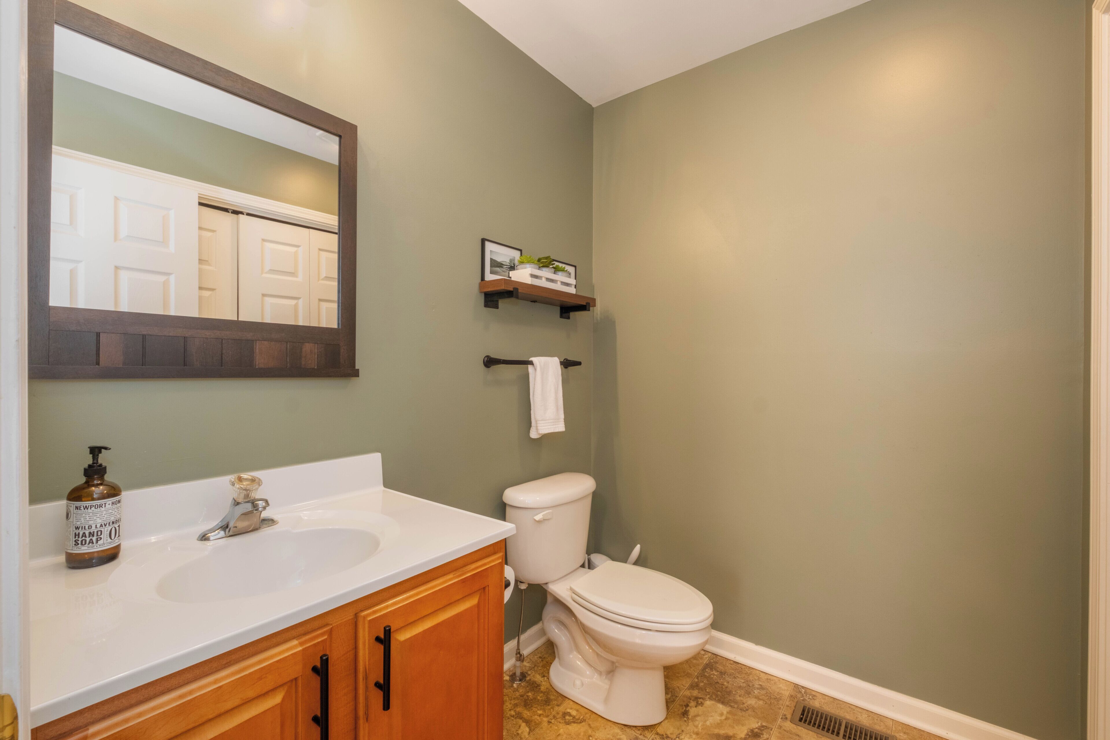 Une salle de bain avec un lavabo blanc, des toilettes, un miroir et une étagère sur laquelle est posée une serviette.
