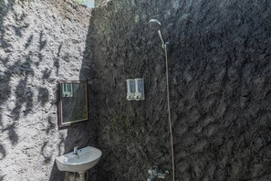 Bathroom features a unique textured wall, sink, mirror, showerhead, and soap dispensers.