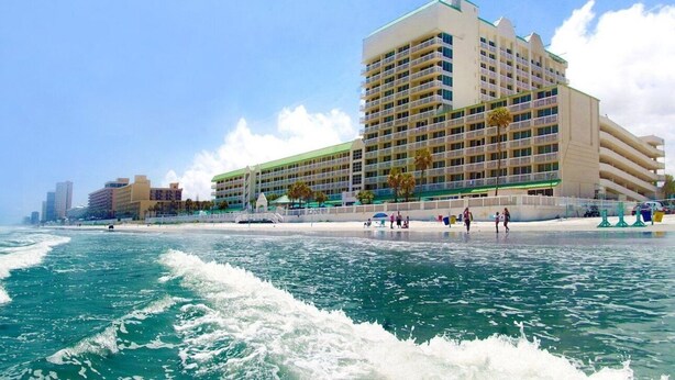 Ein Strandhotel mit mehreren Balkonen, einem Poolbereich und Blick auf den Ozean.
