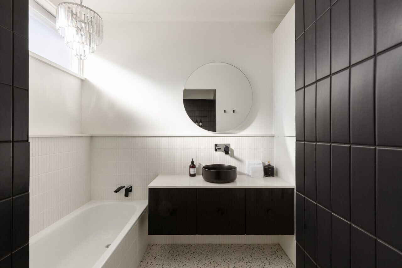 Une salle de bain moderne avec une baignoire sur pieds, un miroir rond et un meuble-lavabo aux tons foncés.