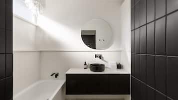 Une salle de bain moderne avec une baignoire sur pieds, un miroir rond et un meuble-lavabo aux tons foncés.