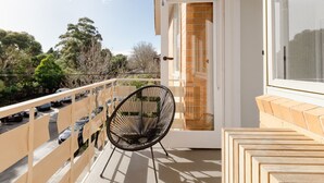 A balcony with a black chair, a glass door, and a view of trees and parked cars.