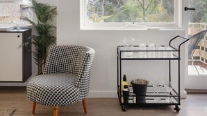 A room with a large window, a houndstooth patterned chair, a metal cart with items, and a plant.