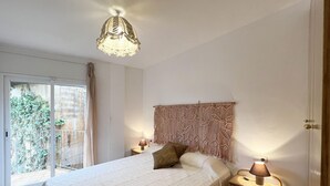 A bedroom with a bed, two bedside tables, a macrame headboard, a hanging light fixture, and a sliding glass door leading to a balcony. - Rental apartment with community pool in Begur (Begur)