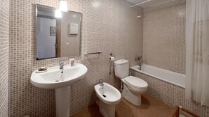 A bathroom with a sink, toilet, bidet, and bathtub, all tiled in a light pattern. - Rental apartment with community pool in Begur (Begur)