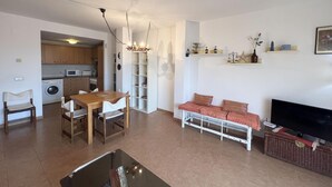 A living room with a TV, sofa, and dining table. There is a kitchen with appliances and cabinets. - Rental apartment with community pool in Begur (Begur)