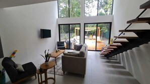 A modern living room with a staircase, a TV mounted on the wall, and a view of the outdoor area. - Modern 2 Bedroom Villa - 10 min. Walk to the Beach (Playa Potrero)