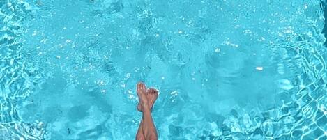 A person relaxing on a wooden deck by a swimming pool.