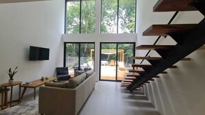 A modern living room with a sofa, a coffee table, and a TV mounted on the wall. There is a staircase leading to an outdoor area with a wooden pergola. - Modern 2 Bedroom Villa - 10 min. Walk to the Beach (Playa Potrero)