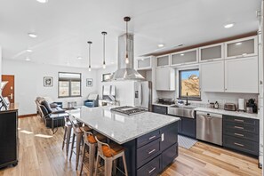 A modern kitchen with a central island, stainless steel appliances, and bar stools. - Modern 5bd mins from downtown (Great Falls)