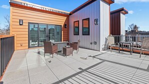 Ein modernes Gebäude mit einer Terrassenfläche, die Gartenmöbel und einen Blick auf eine entfernte Struktur bietet.