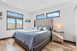 Une chambre avec un grand lit, deux fenêtres, une table de chevet et une lampe fixée au mur.