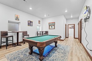 Une table de billard dans une pièce dont le sol est recouvert de parquet, avec un tapis bleu et des affiches encadrées accrochées aux murs.