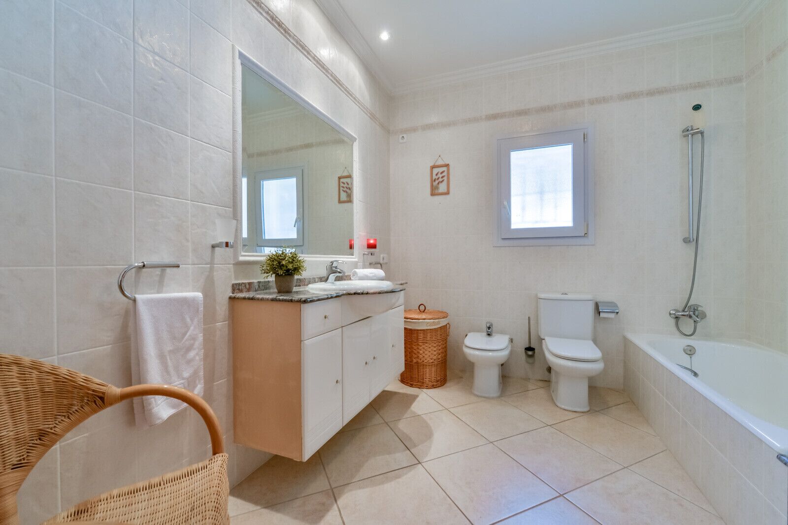 A modern bathroom with a large mirror, two toilets, a bathtub, and a wicker chair.