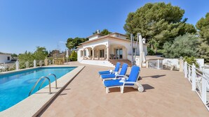 A pool area with a clear blue pool, a white building with columns, and blue lounge chairs. - Villa MyPlaceToBe Moraira (Moraira)