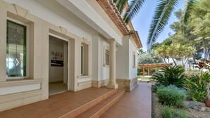 A building with a tiled entrance, a covered patio area, and a garden with various plants. - Villa MyPlaceToBe Moraira (Moraira)