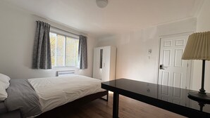Un dormitorio con cama, escritorio, armario y ventana con cortinas.