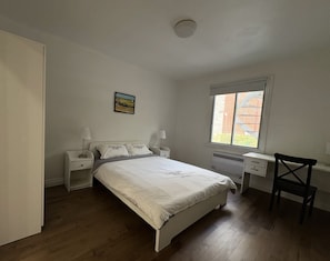 A bedroom with a bed, bedside tables, a desk, and a chair.