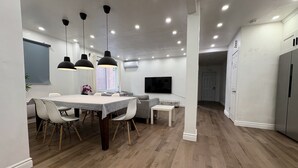 Una cocina moderna con comedor, suelo de madera, iluminación colgante y un televisor montado en la pared.