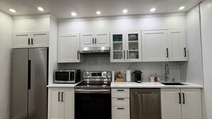 Una cocina moderna con electrodomésticos de acero inoxidable, armarios blancos e iluminación empotrada en el techo.