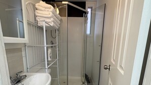 Un baño pequeño con lavamanos blanco, inodoro y ducha con mampara de vidrio.