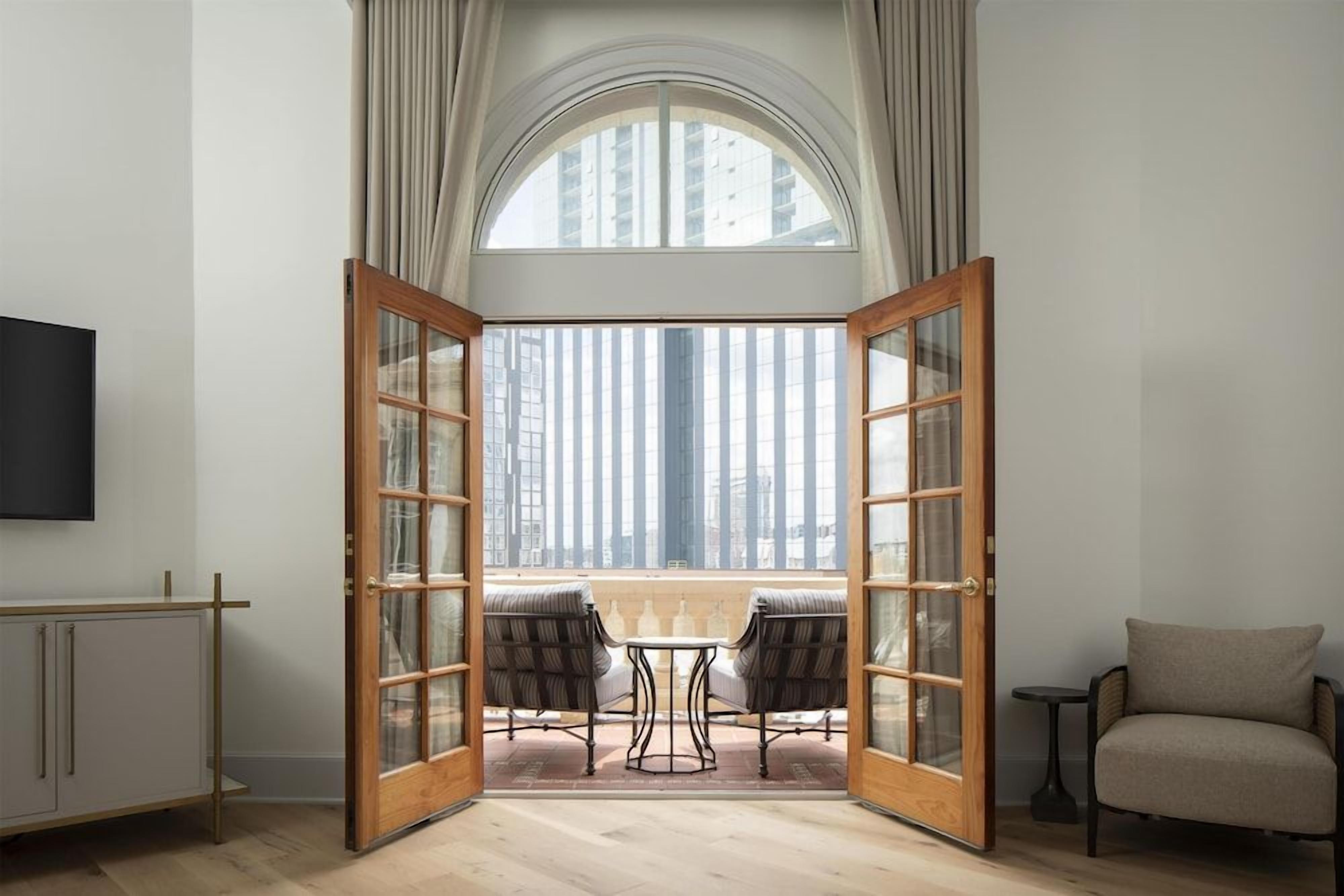 Ein Zimmer mit einem großen Bogenfenster, einer Holztür mit Glasfeldern, einem kleinen Tisch mit zwei Stühlen und einem Sofa.