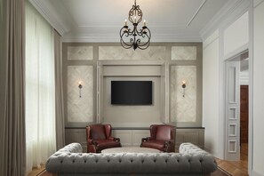 Un salon doté d’un grand téléviseur à écran plat fixé au mur, de deux fauteuils en cuir, d’un pouf capitonné et d’un lustre.