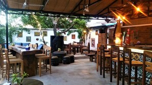 An outdoor dining area with wooden tables and chairs, a bar with a counter, and a Buddha statue. - Sleeping Angkor Hotel (Siem Reap)