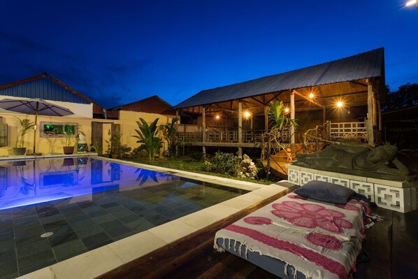 A poolside area with a bed, a covered deck, and a building with a metal roof. - Sleeping Angkor Hotel (Siem Reap)
