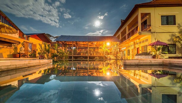 A serene pool reflecting the night sky, surrounded by traditional buildings with balconies and potted plants. - Sleeping Angkor Hotel (Siem Reap)