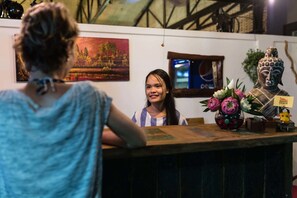 A reception area with a wooden counter, a Buddha statue, and a painting of a temple. - Sleeping Angkor Hotel (Siem Reap)