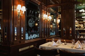 L’intérieur d’un restaurant avec des boiseries, des lustres et une table dressée pour le dîner.