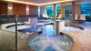 Een wellnessruimte met verschillende bubbelbaden, ligstoelen en een stenen vloer.