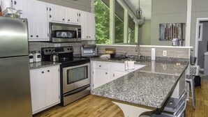Una cocina moderna con armarios blancos, electrodomésticos de acero inoxidable, encimera de granito y un amplio ventanal que proporciona luz natural.