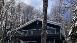 Un chalet de dos pisos con balcón, rodeado de árboles cubiertos de nieve y un cielo despejado.