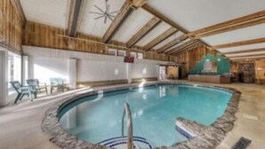 Una piscina interior con techo y paredes de madera, rodeada de sillones de descanso.