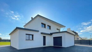 Una casa de dues plantes amb garatge, teulada plana i cel serè.