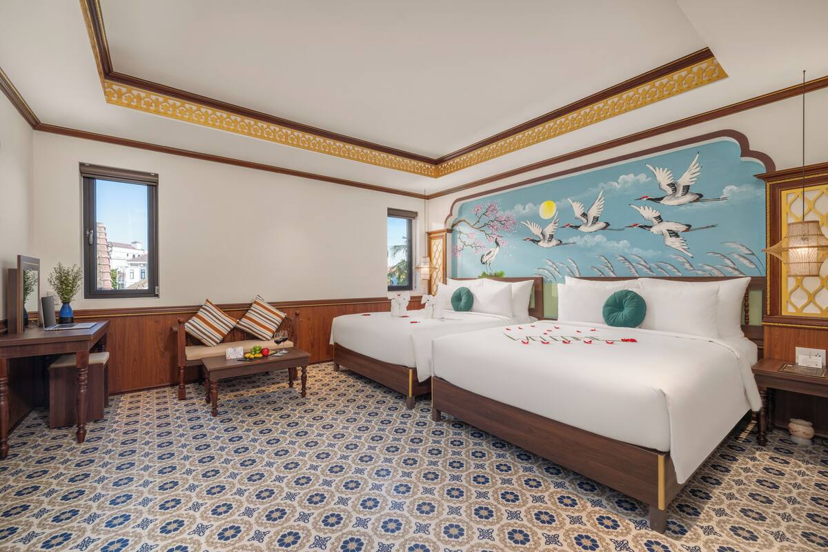 A hotel room with two beds, a desk, a chair, and a patterned floor.