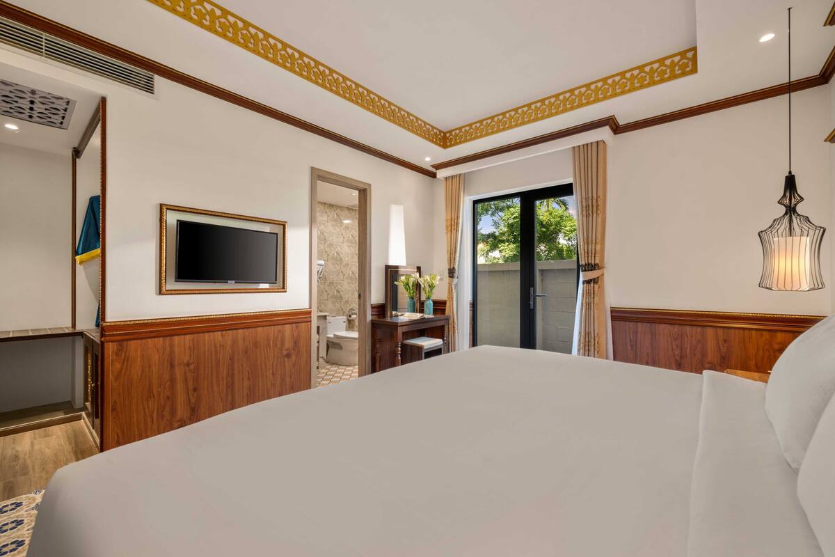 A hotel room with a large bed, a television, a desk, and a bathroom visible through an open door.