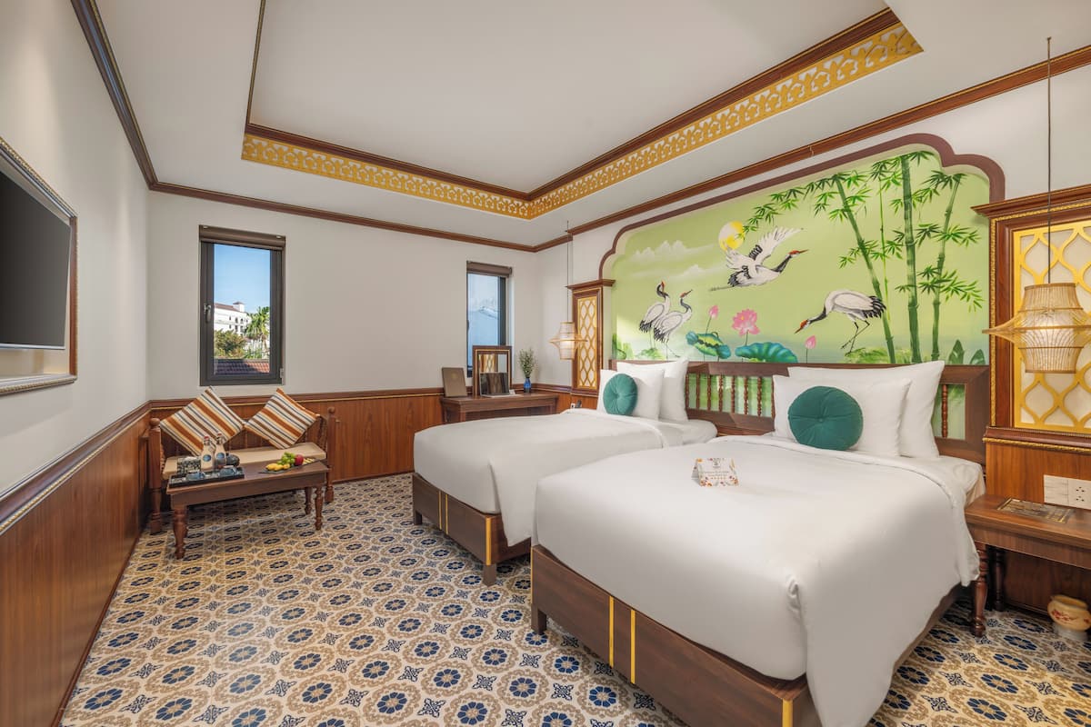 A hotel room with two beds, a wooden sofa, patterned floor, and a mural with birds and bamboo.